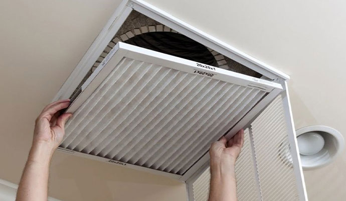 Person installing a clean pleated air filter into a ceiling HVAC return vent