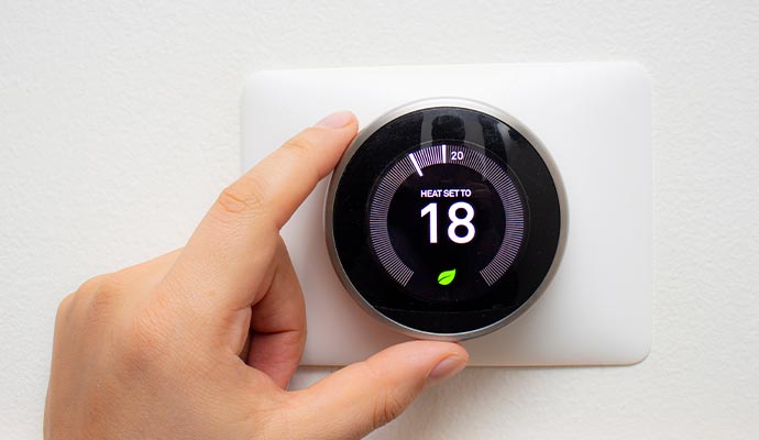 A hand adjusting a smart thermostat mounted on a wall