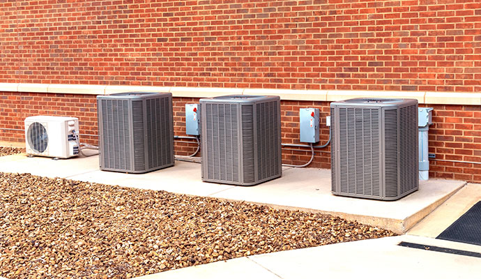 Commercial HVAC condenser units positioned in a row against a brick wall