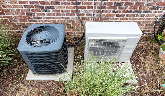 Two types of central air conditioning units positioned outside a brick residential building