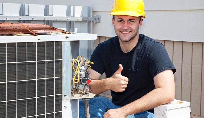 A smiling HVAC technician giving a thumbs-up next to an outdoor AC unit A smiling HVAC technician giving a thumbs-up next to an outdoor AC unit