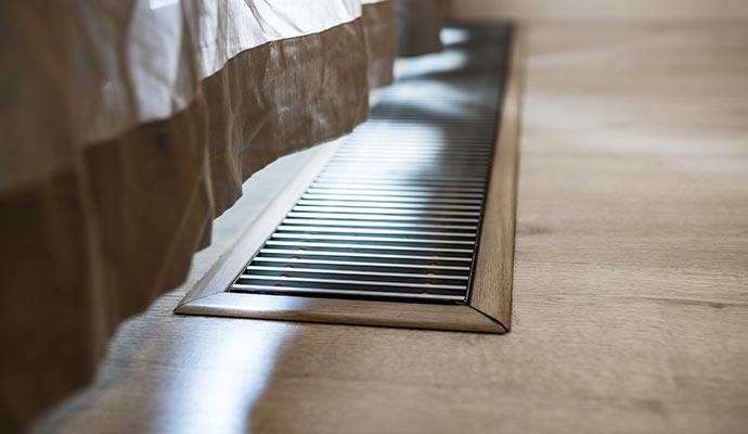 A close-up of a metal HVAC air vent set into a light wood floor