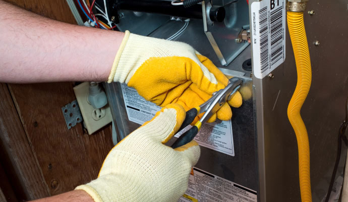 Technician wearing work gloves using pliers to repair heating furnace equipment