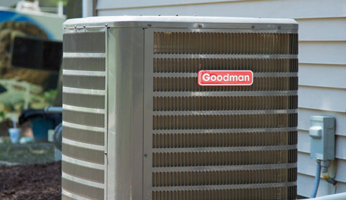 A Goodman air
          conditioning condenser unit installed outside a residential home