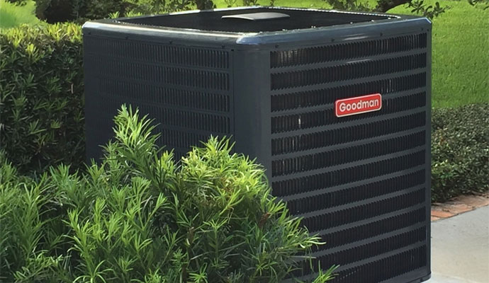 A Goodman outdoor air conditioning unit installed in a backyard with green landscaping in West Palm Beach
