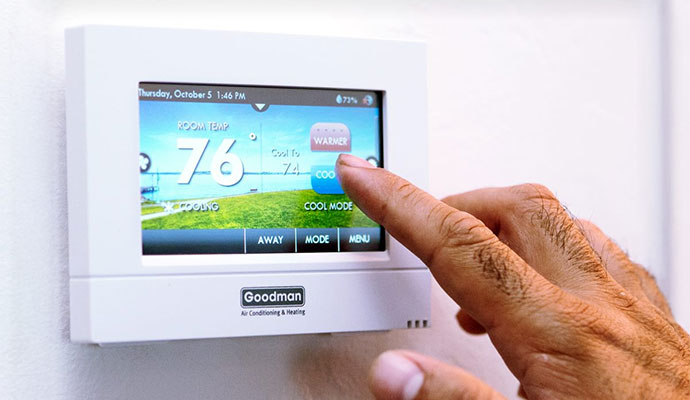 A hand touching the digital screen of a Goodman smart thermostat to adjust the home temperature settings