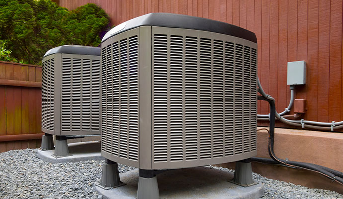 Two outdoor HVAC heating and air conditioning condenser units on gravel pads