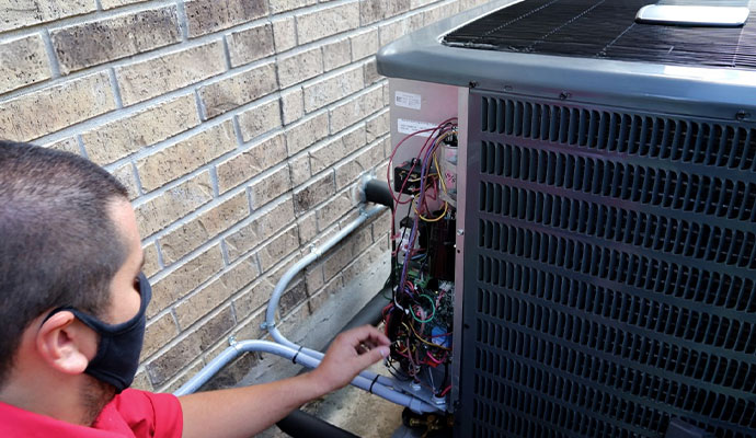 HVAC technician inspecting the electrical wiring of an outdoor air conditioning unit during a proper installation