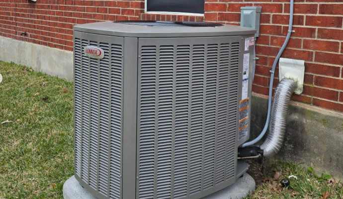 A Lennox outdoor air conditioning condenser unit installed on a concrete pad next to a brick house