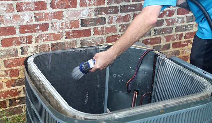 Technician spraying water inside outdoor air conditioning unit to clean coils