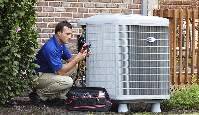 Professional HVAC technician with tools inspecting an outdoor heating and cooling unit