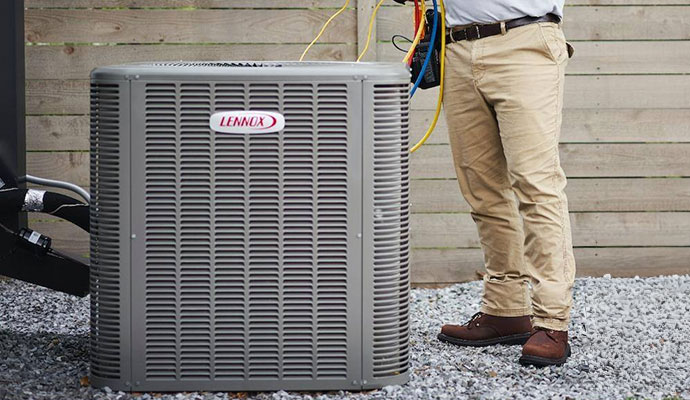 A technician standing next to a Lennox outdoor air conditioning unit performing regular maintenance