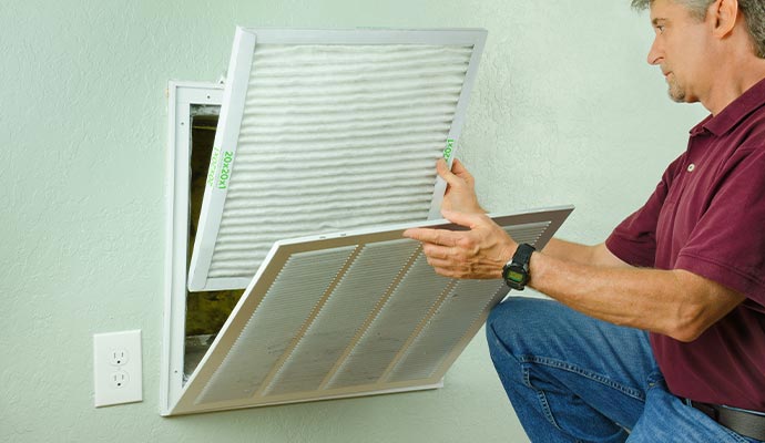 Person replacing an air filter in a wall-mounted air return vent