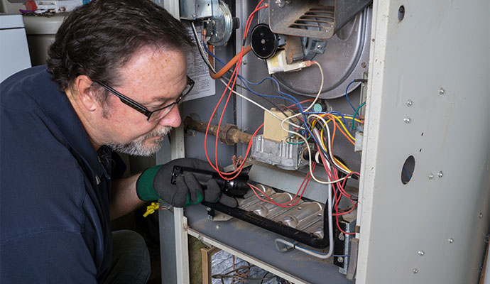 HVAC technician using a flashlight to inspect internal furnace components